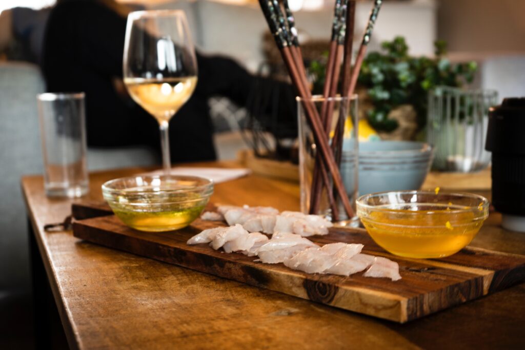 Fish on a wood board with a glass of wine and dipping sauce.