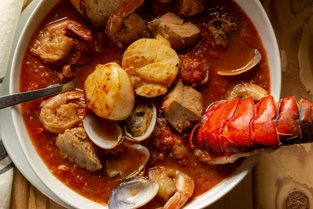 Cioppino in a white bowl with a lobster tail sticking out.