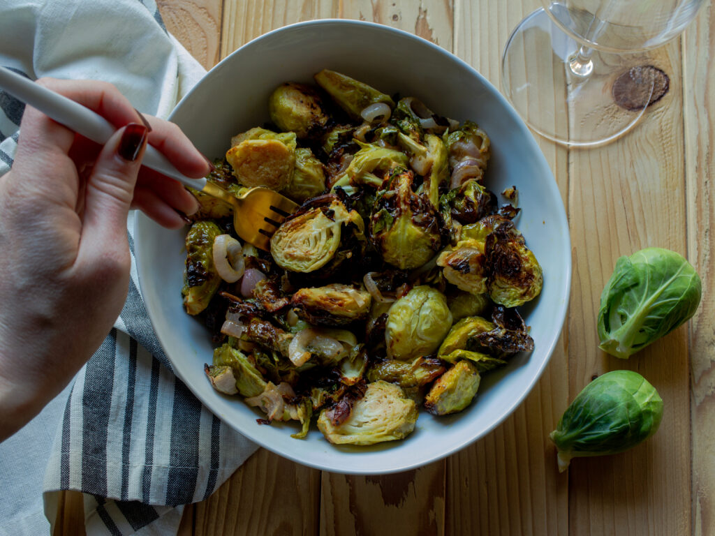 Air fryer brussels sprouts in a white bowl with a hand holding a fork that is grabbing a brussel sprout.