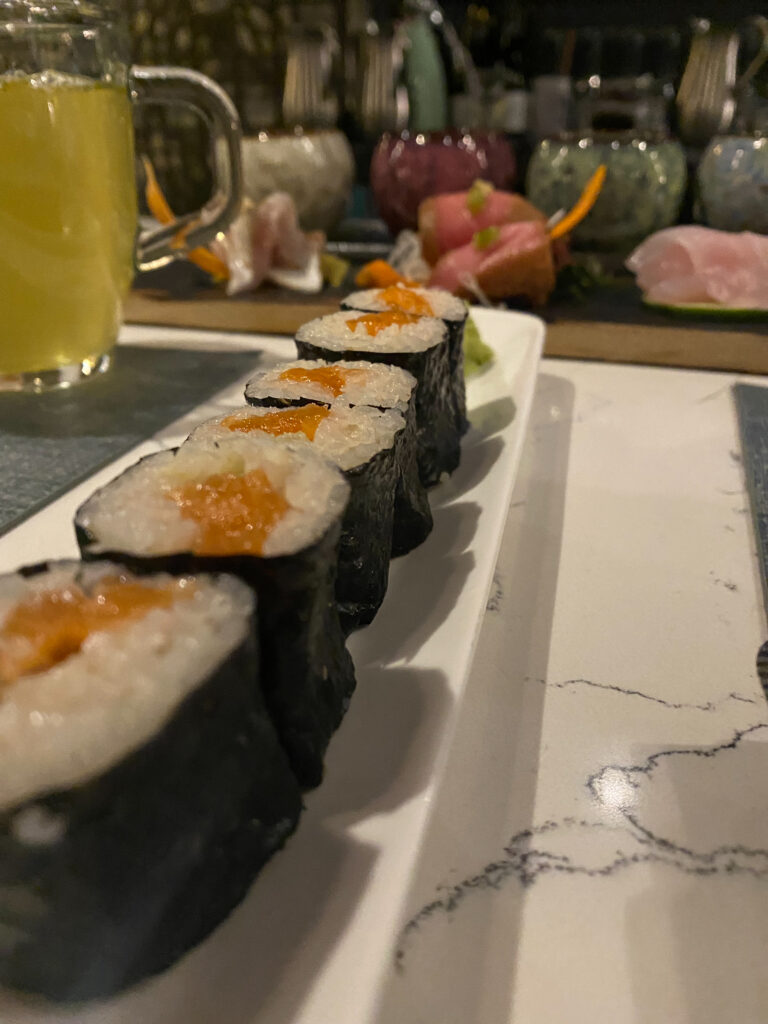 A salmon roll on a white plate next to a mug of green tea.
