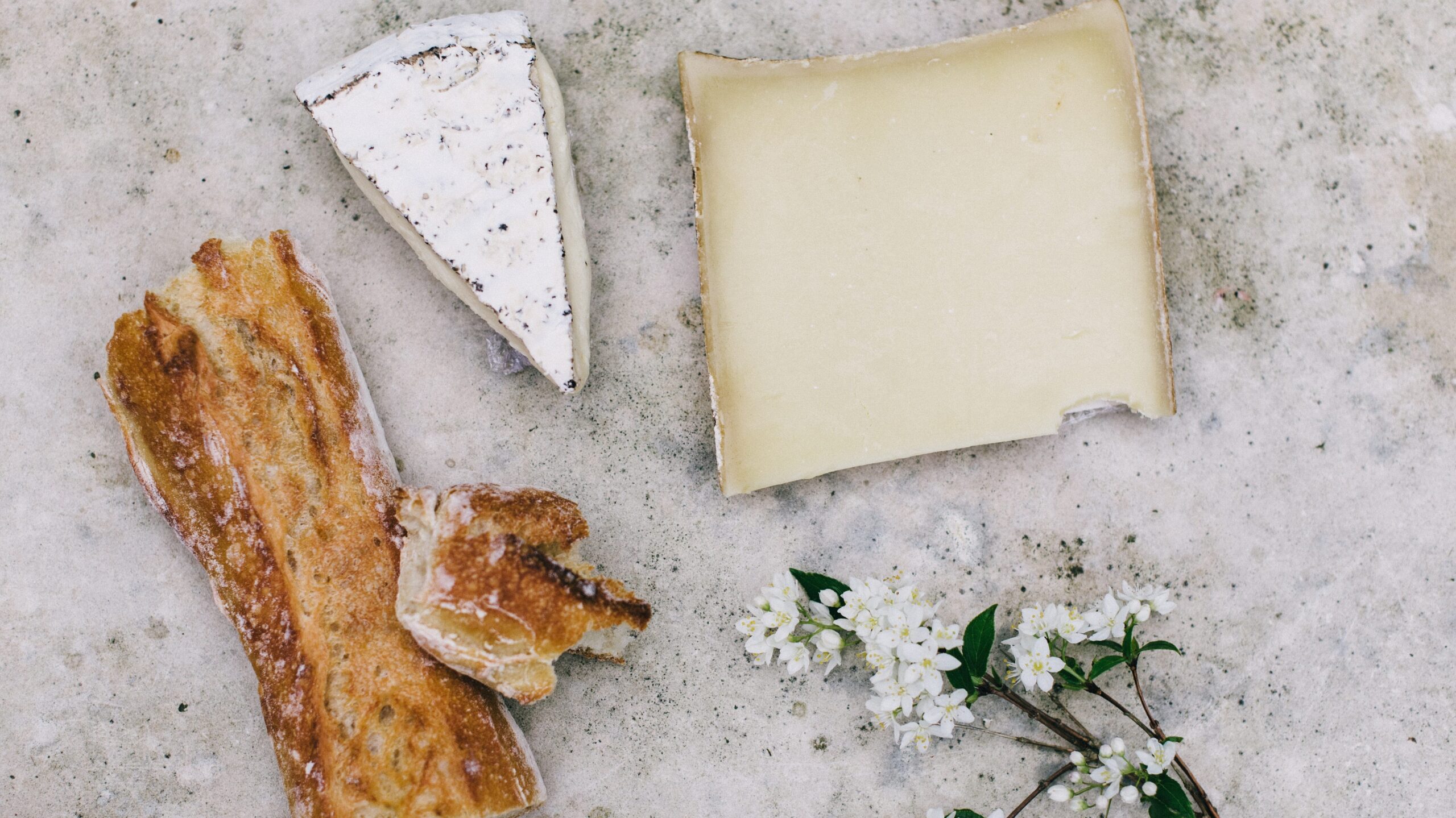 Two wedges of cheese, a sprig of flowers, and a baguette with a bite ripped out of it.
