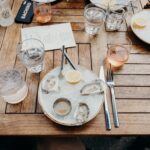 A plate of oysters next to water glasses and a glass of rosé wine.